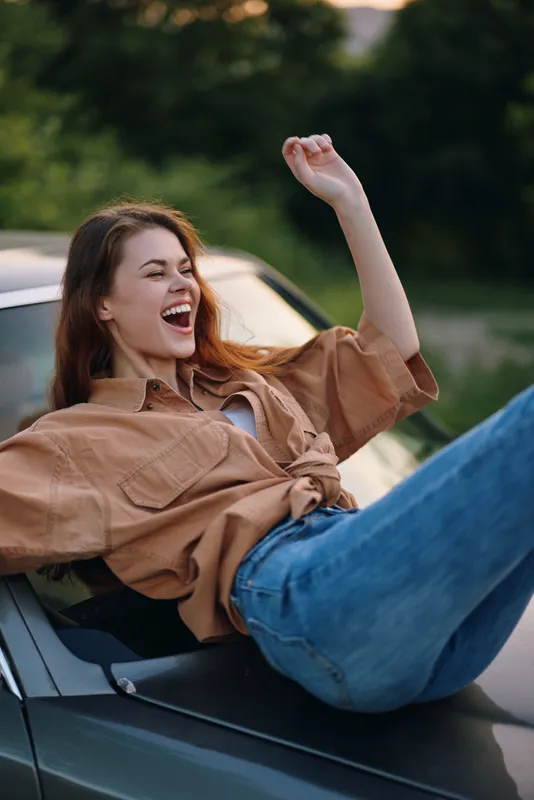 Happy young woman enjoying a carefree moment outdoors in a stylish outfit, emphasizing joy and freedom with her laughter.