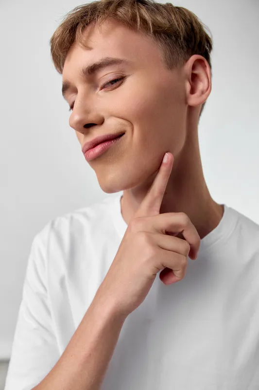 Thinking gesture with chin touch, cheerful male in white shirt, confident expression and thoughtful pose for lifestyle photography with bright studio lighting