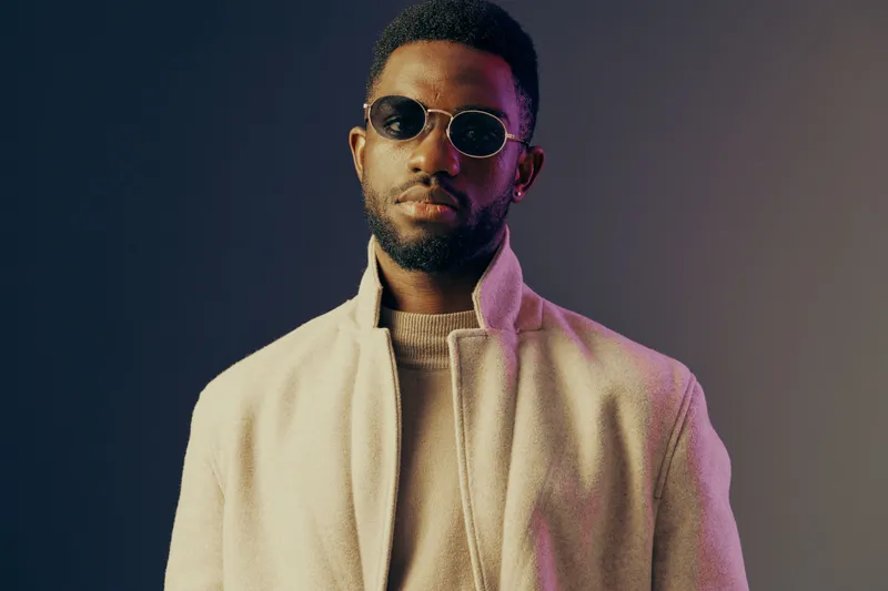 Stylish young African man in sunglasses wearing a fashionable coat against a gradient background, exuding confidence and contemporary vibe