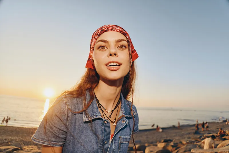 lifestyle woman in modern boho-western denim street style captured at sunset on beach with warm film color tones and relaxed natural expression