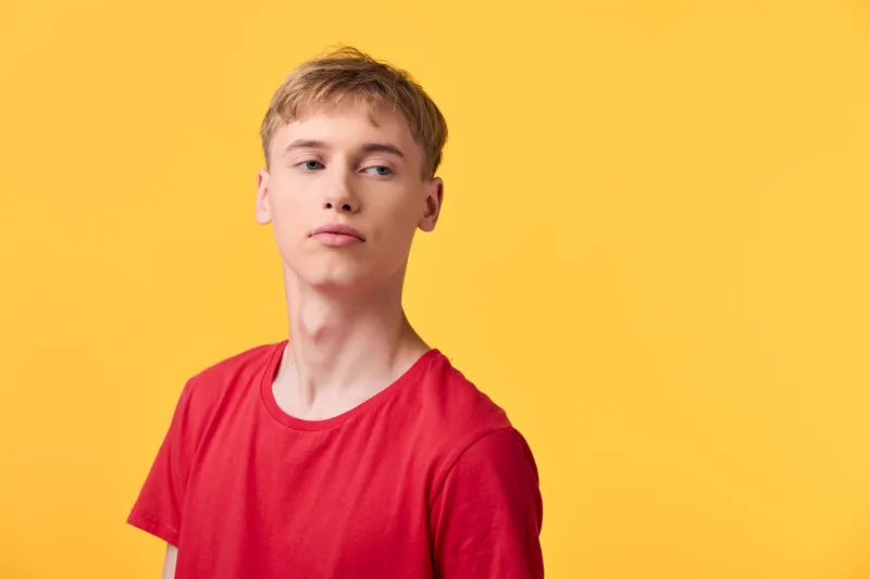 Young man in a red shirt stands against a vivid yellow backdrop, casual pose, clean lines, fashion mood, studio style, vibrant color contrast, contemporary lifestyle image with confident expression
