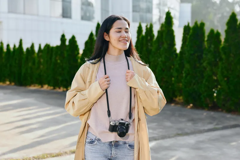 woman, camera, outdoor, smiling, casual, fashion, jacket, sweater, jeans, daylight, photography, lifestyle, street, streetstyle, accessory, greenery, urban, sunny, natural, leisure, travel, candid,