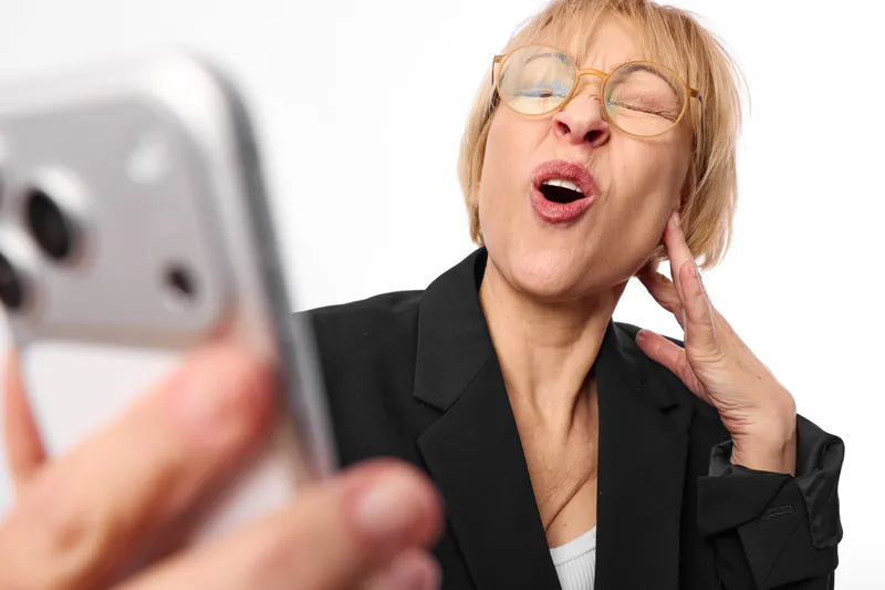 Elderly business woman portrait, surprised expression holding smartphone near face, eyeglasses, indoor studio on white background, tech communication moment concept today
