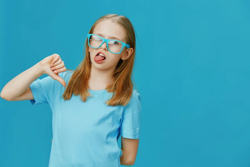 A young girl with glasses making a silly face against a bright blue background, expressing playful emotions in a vibrant, fun atmosphere
