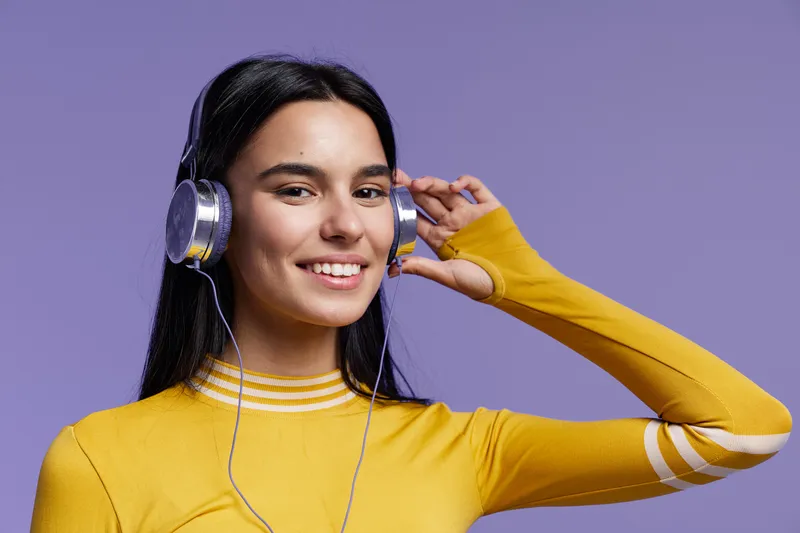 young woman sport fitness listening to music with headphones, smiling and wearing yellow sweater on purple background, healthy lifestyle concept