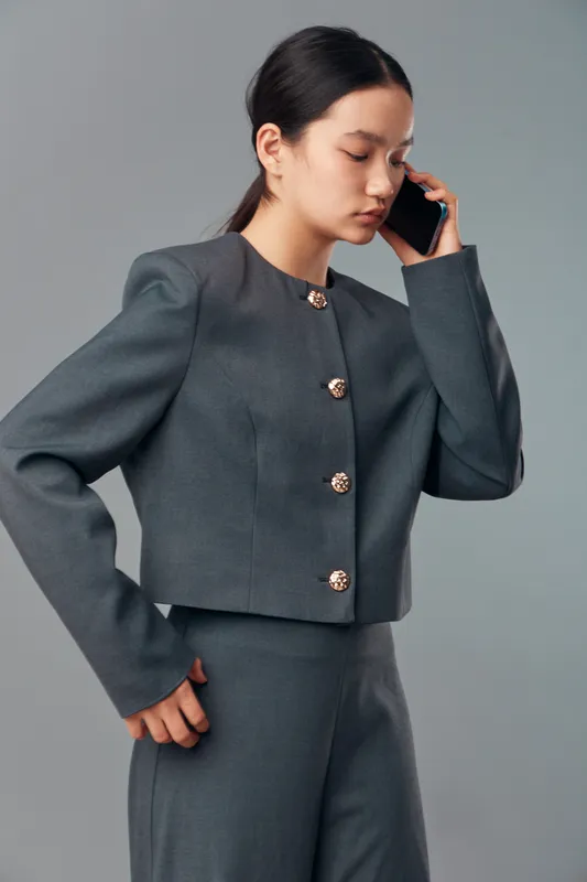 Woman in gray suit standing and talking on mobile phone with serious expression in studio. Female professional, communication and technology for business call and corporate style fashion.