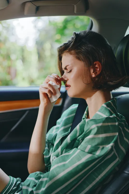 Relaxed woman sits in a parked car with eyes closed and hand near her face, wearing a green striped shirt.