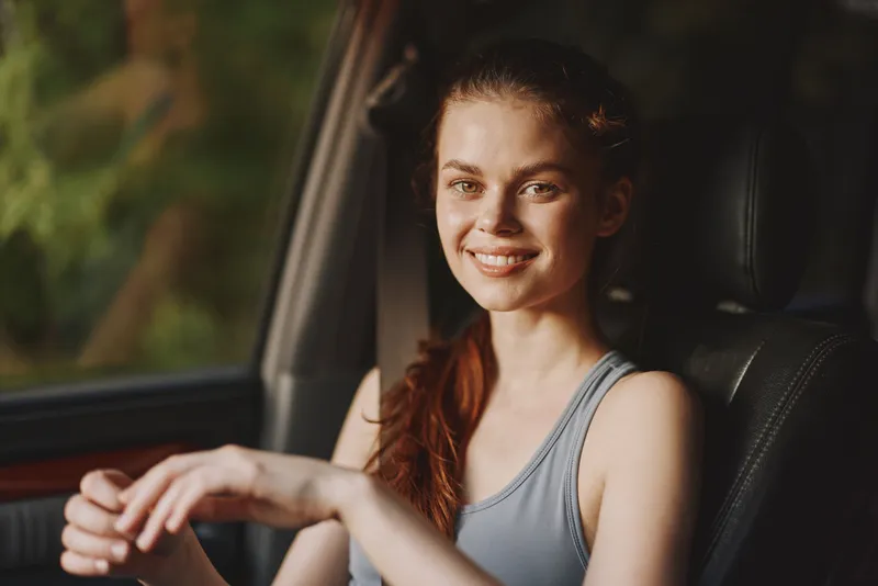 Smiling young woman in sportswear sitting in a car, natural light, expressing happiness and relaxation, suitable for fitness and lifestyle concepts