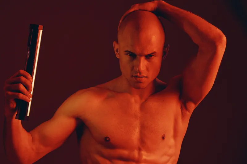 Strong man posing with an intense expression in a monochromatic, red-lit setting, showcasing powerful emotions and artistic composition.