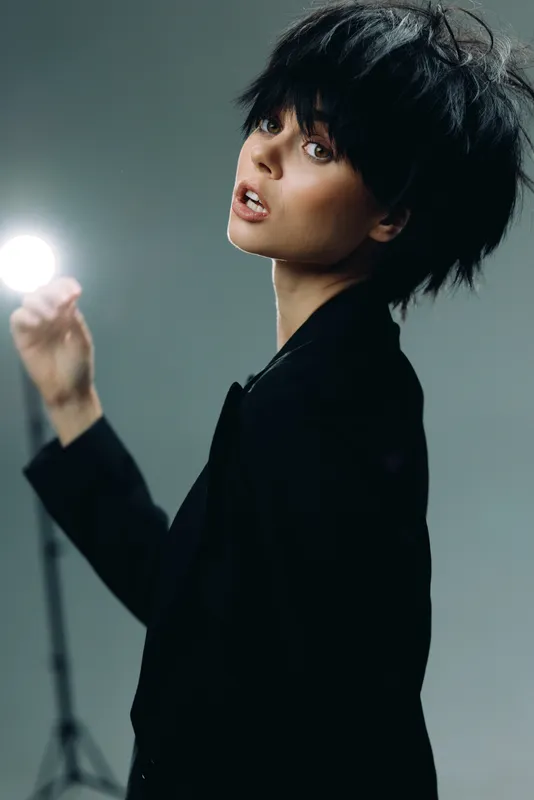 Young woman with short black hair holding bright light in dark studio setting with moody atmosphere
