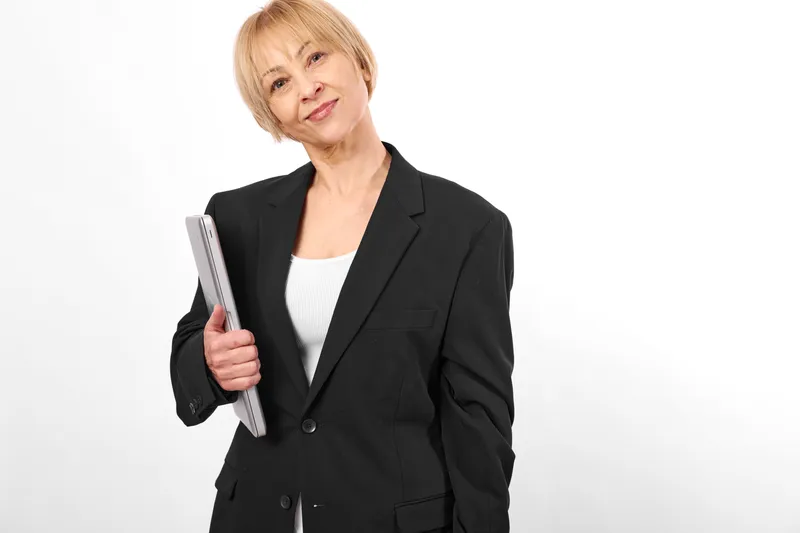 Elderly woman in black suit holding a book, portrait on white background, calm thoughtful smile, education and learning concept, isolated studio shot