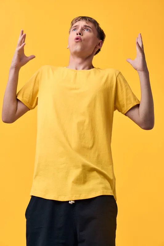 Surprised man in a yellow T-shirt raises hands in astonishment against a bright yellow backdrop, conveying expressive emotion and dynamic reaction for lifestyle and fashion stock.