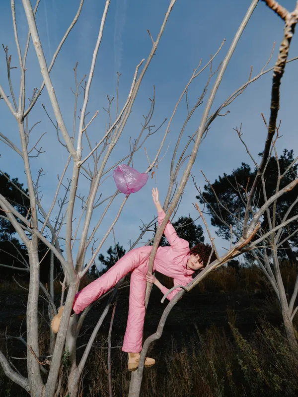 Young child climbing a bare tree outdoors in pink clothing exploring nature and playing high among branches under a clear blue sky