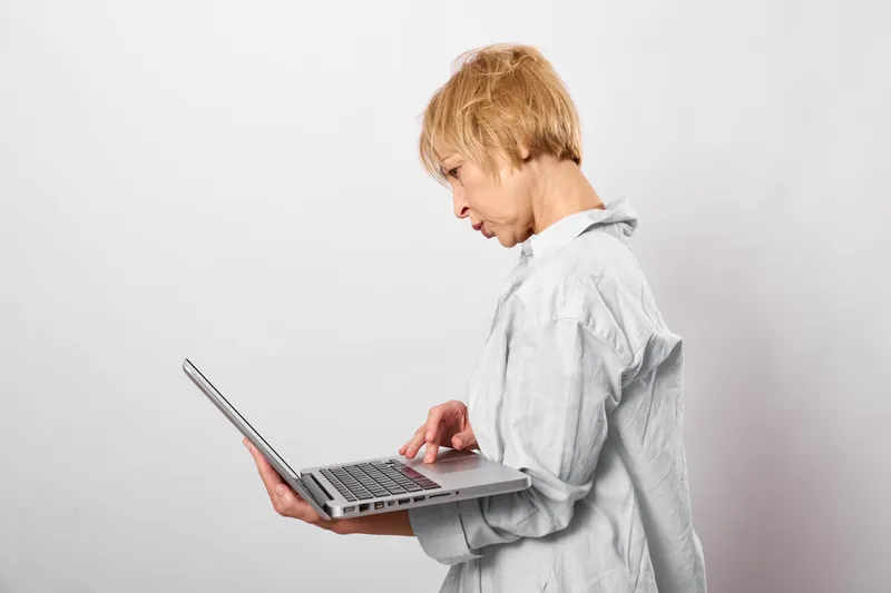 Woman with laptop in a clean studio, head down with stress and tired expression, typing for remote work, concept of burnout and mental pressure, during deadline, copy space today