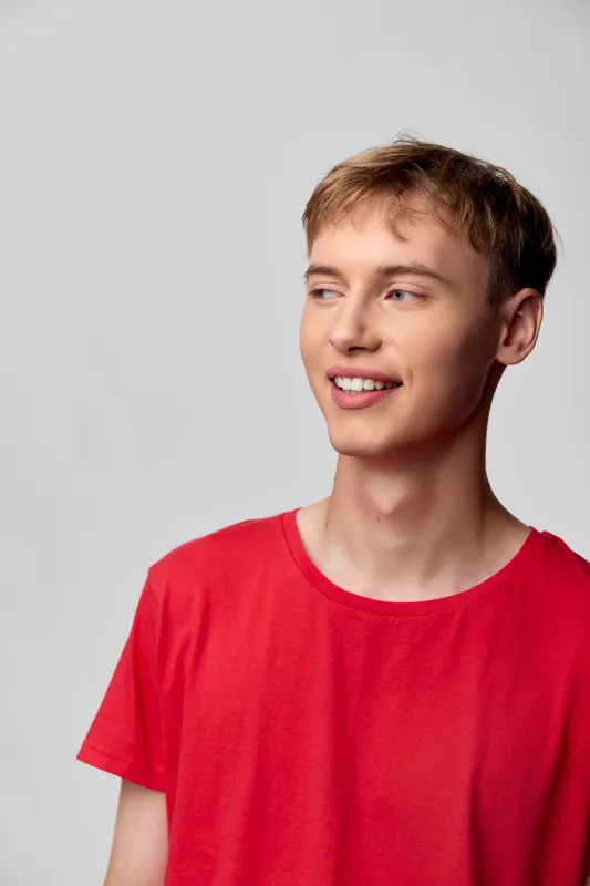 Smiling young man in a red shirt, casual fashion in a studio with neutral backdrop and bright lighting, relaxed pose, clean composition, modern style and friendly vibe