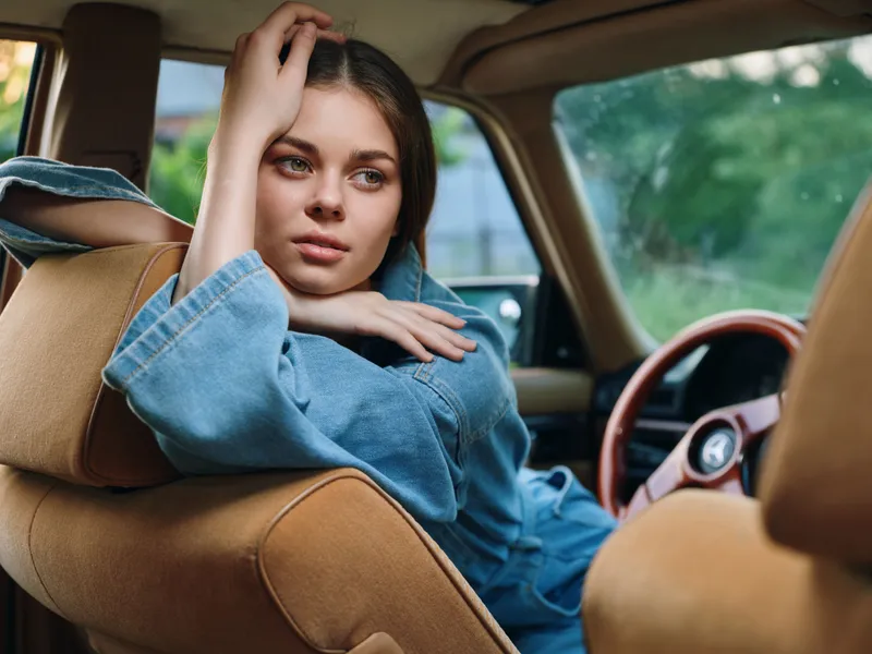 Young woman in casual denim outfit resting in car, expressing serenity and contemplation against a vibrant green background.
