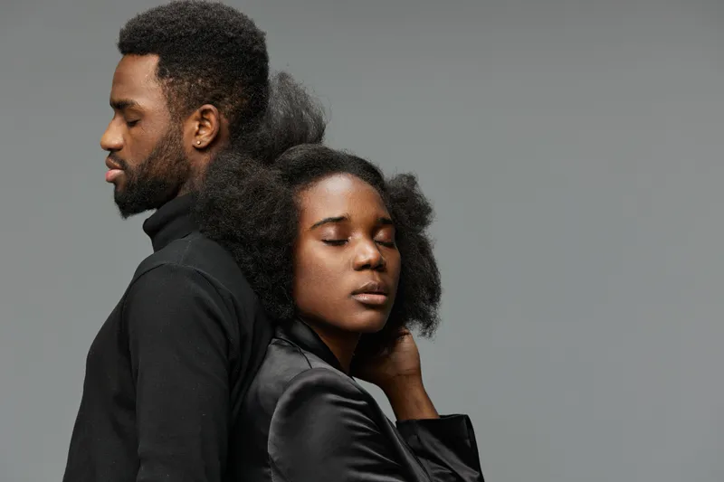 A striking portrait of a Black couple showcasing natural hairstyles, conveying intimacy and confidence against a minimalistic gray background