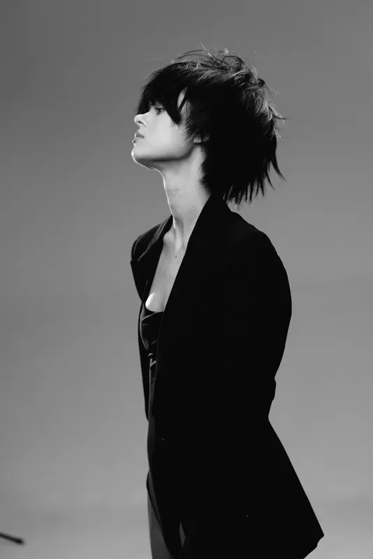 Black and white portrait of a woman with short hair wearing a blazer looking sideways in a studio.