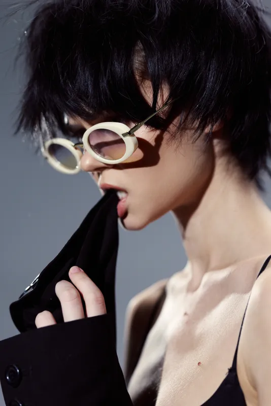 Young woman wearing round glasses biting black fabric with stylish messy hair in neutral tones