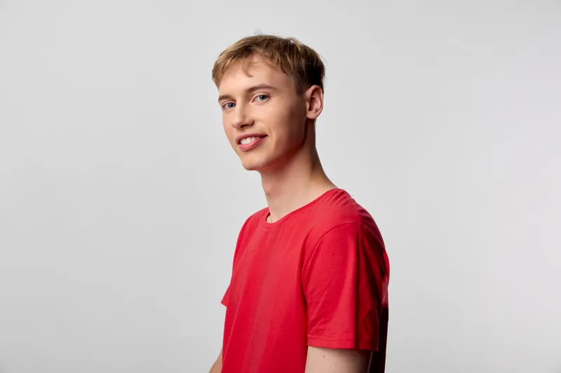 Male, young, smiling in a red shirt in a clean studio setting, side profile with soft lighting, casual mood, approachable vibe, suitable for lifestyle and fashion campaigns and commercial projects