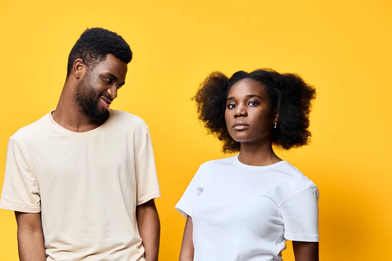 Young diverse couple against a vibrant yellow background displaying playful emotions and trendy casual outfits reflecting modern relationship dynamics
