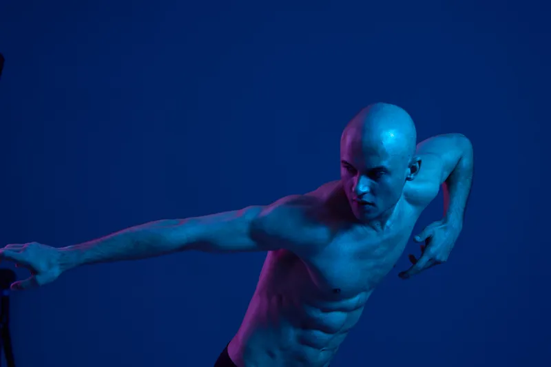 Captivating man in dynamic pose, showcasing strength and grace against a blue backdrop, highlighting his toned physique and expressive movement.