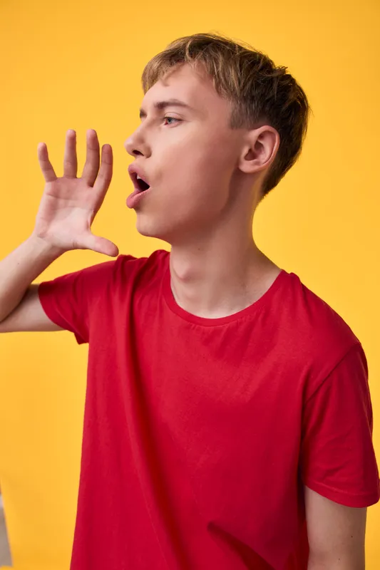 Boy shouting with hand near mouth red shirt against yellow background conveying energy and urgency suitable for communication advertising and attention grabbing stock photo