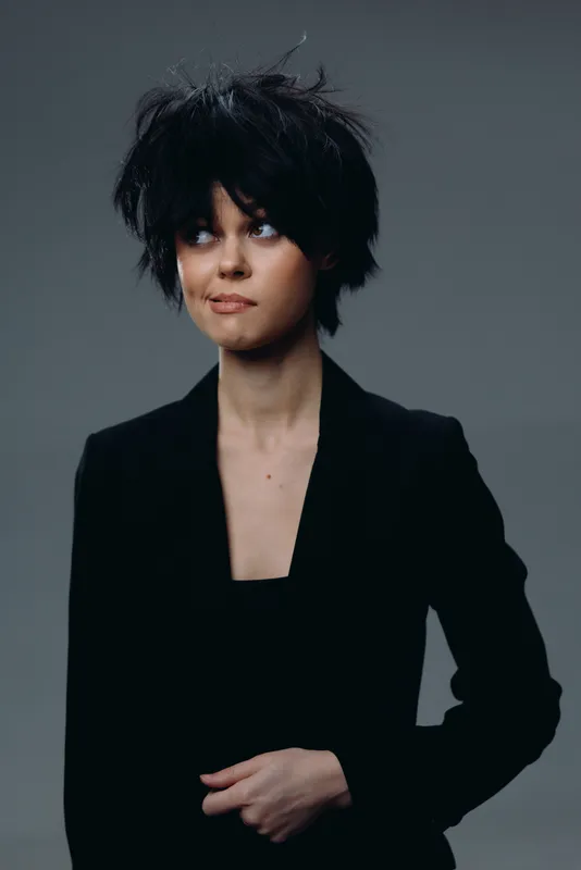 Young woman with short messy black hair wearing black blazer looking aside
