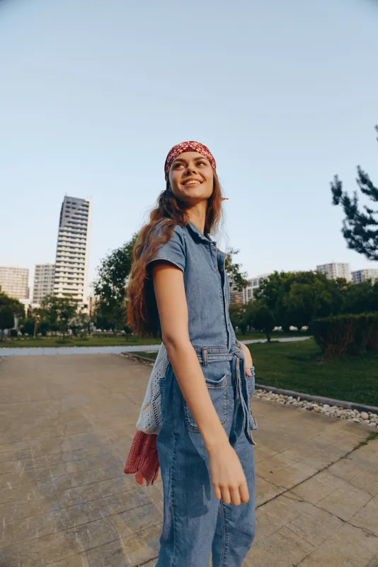 Lifestyle woman in modern boho-western denim street style smiling outdoors in urban park, film color, casual fashion, young joyful confident woman.