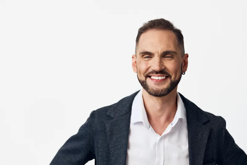 Professional man with a confident, warm smile stands before an isolated colored background, conveying modern business poise, approachability, and strong focus in a corporate setting.