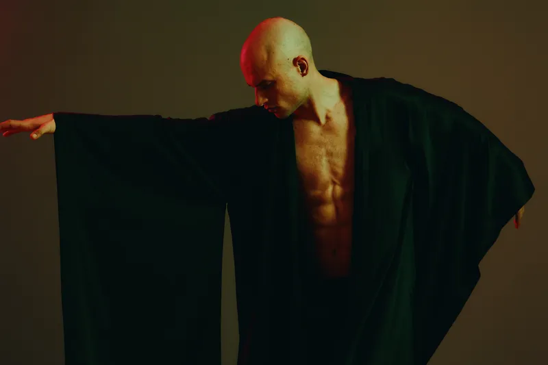 Artistic portrait of a man striking a dynamic pose, showcasing his athletic physique and black attire. The image conveys a sense of strength and movement.