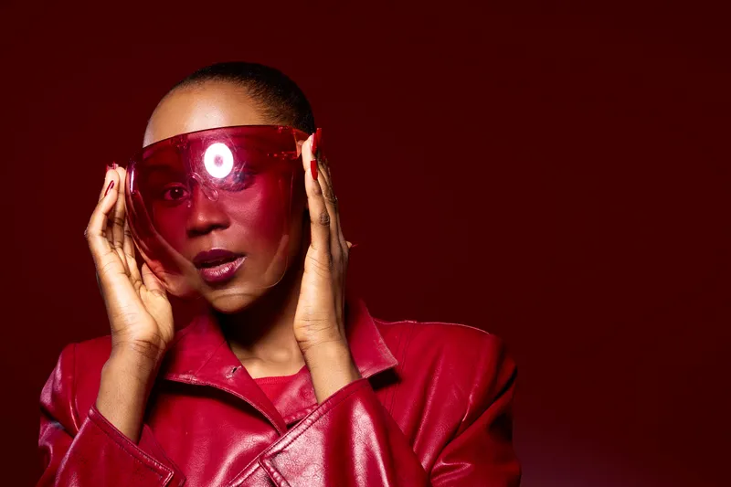 Confident African American woman with dark skin wearing red leather jacket and large red sunglasses. Studio portrait on red background. Concept of fashion, style, and bold accessories.