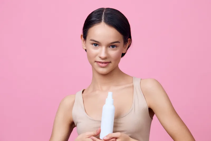 Young female model holding a skincare product against a pink background, embodying beauty and confidence, ideal for wellness and personal care themes