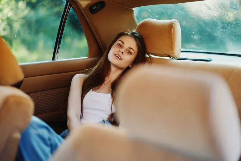 Young woman relaxing in a car, portraying calmness and serenity, dressed casually in a tank top, with soft natural light flooding the interior.