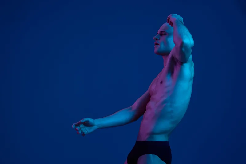 Artistic portrait of a man in dramatic lighting, showcasing his physique with a captivating pose and modern expression, emphasizing the emotional impact of the moment.