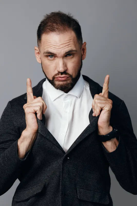 Professional man in a tailored suit stands against a solid colored background, projecting confidence and focus while showing subtle emotion through a keen gaze and poised posture.
