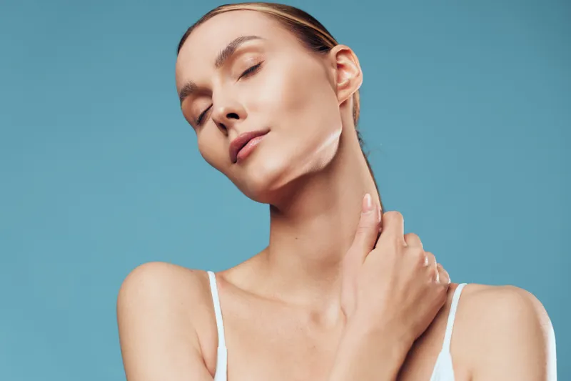 Woman in skincare beauty scene, applying cream to face, calm wellness and selfcare, studio closeup on blue background, gentle light, soft skin texture