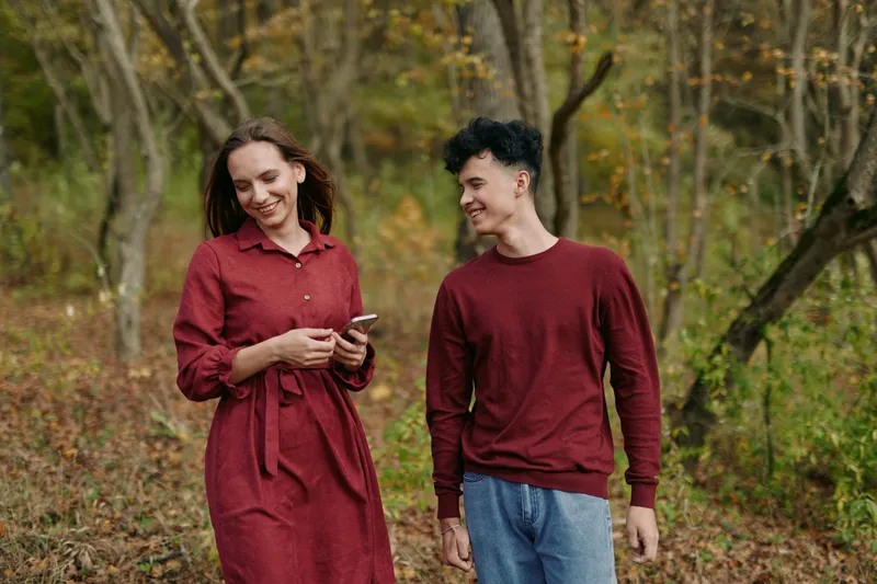 Authenticity and credibility are reflected in an outdoor candid moment as a couple walks through autumn woods, smiling naturally, wearing simple clothing, sharing quiet dialogue, and enjoying unposed