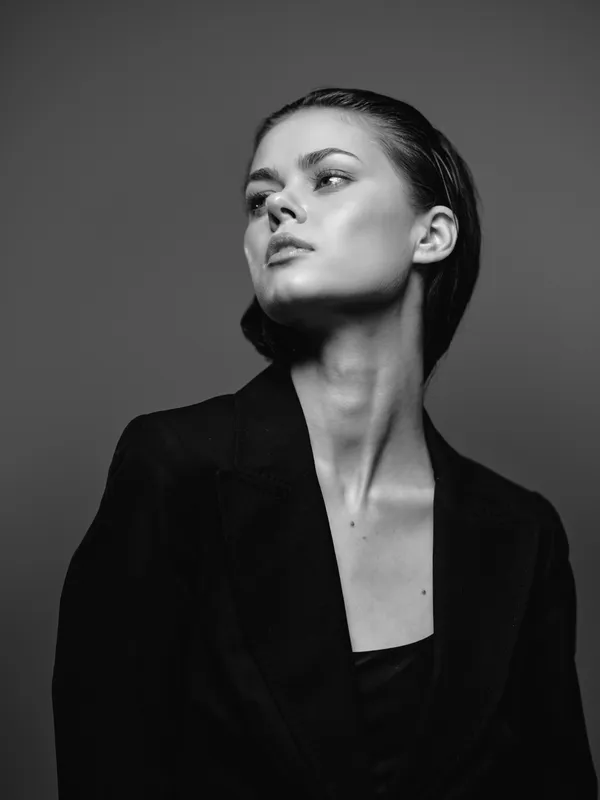Black and white portrait of a confident woman in a dark blazer with a thoughtful expression and minimalist style.