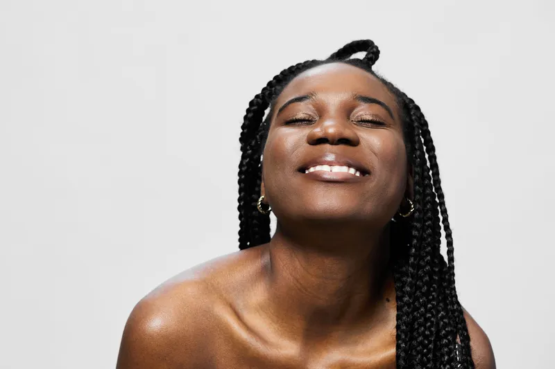 Joyful African woman with braided hair smiling against a bright background, showcasing happiness and confidence for beauty and self care concepts