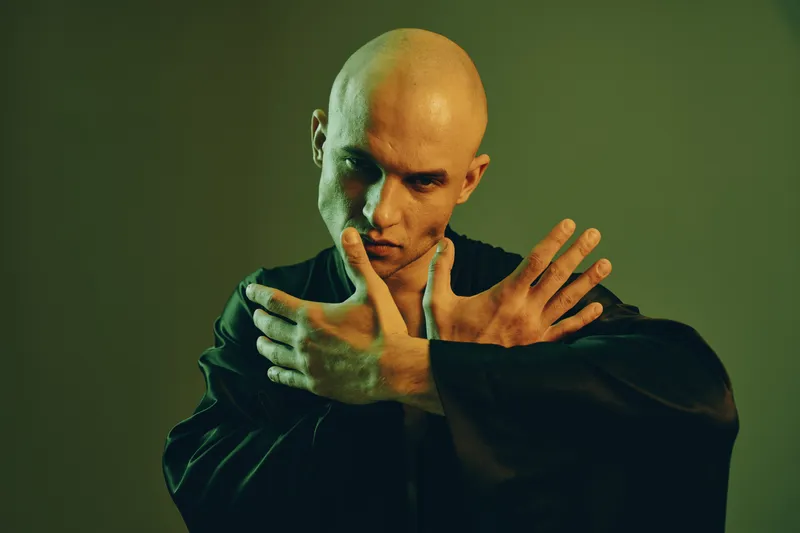 Introspective man poses dramatically in a dimly lit setting, expressing deep emotions with a unique artistic flair. A striking blend of light and shadow enhances the scene.