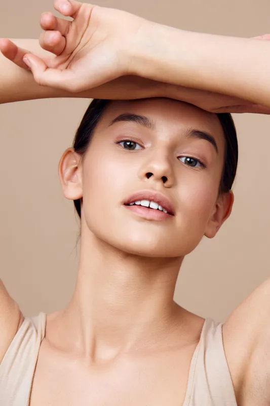Young woman with natural makeup posing against a neutral background, showcasing fresh beauty and confidence in a minimalist style, ideal for lifestyle and skincare concepts