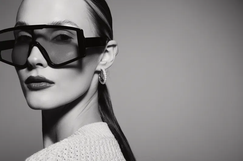 Portrait of a white woman with pale skin wearing oversized modern sunglasses and hoop earrings in studio lighting.