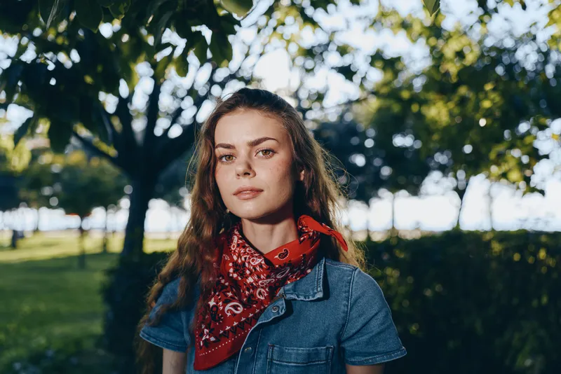 lifestyle woman wearing modern boho-western denim and red bandana in street style with natural sunlight and film color effect, outdoors in a park setting