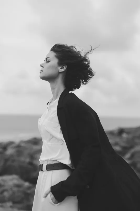 woman, wind, beach, coat, profile, black, windblown, serene mood, outdoor fashion, sea breeze, monochrome silhouette by the shore, dramatic sky and rugged coast