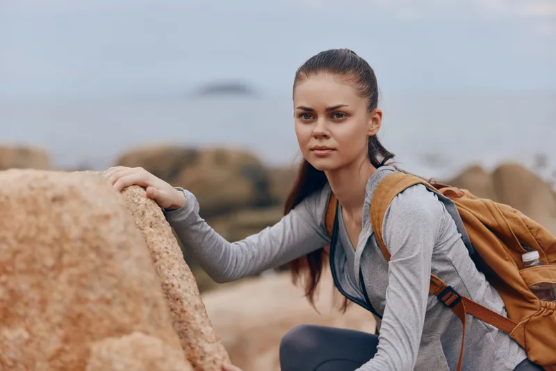 Young woman in athletic wear exploring rocky coastline with a backpack, showcasing determination and adventure in a serene outdoor setting