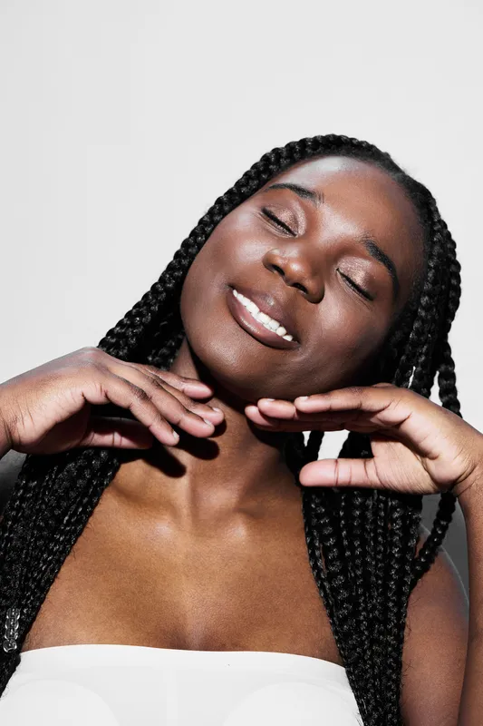 Beautiful African woman with braided hair expressing joy against a neutral background in a bright, uplifting atmosphere, emphasizing confidence and happiness