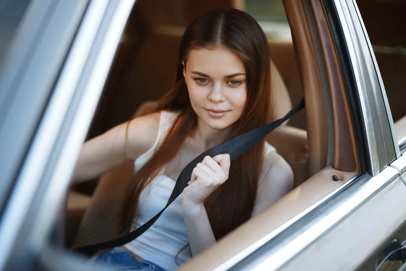 Young woman with long hair fastening seatbelt in a car, wearing a casual outfit, displaying a calm expression, emphasizing safety and comfort in a urban setting.