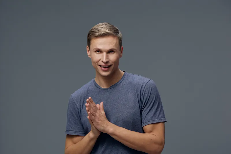 Man smiling cheerful young Caucasian male in casual blue t-shirt looking happy with friendly expression isolated on solid gray background in studio portrait. People lifestyle concept
