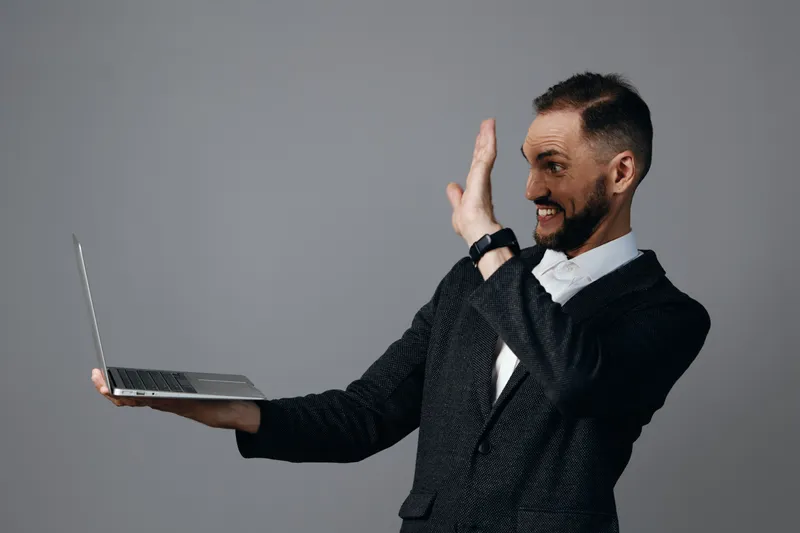 A professional business man on an isolated colored background, smiling as he waves with a laptop, conveying confidence, energy, and engaging communication.